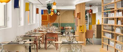 A modern restaurant with round tables, chairs, and hanging pendant lights.