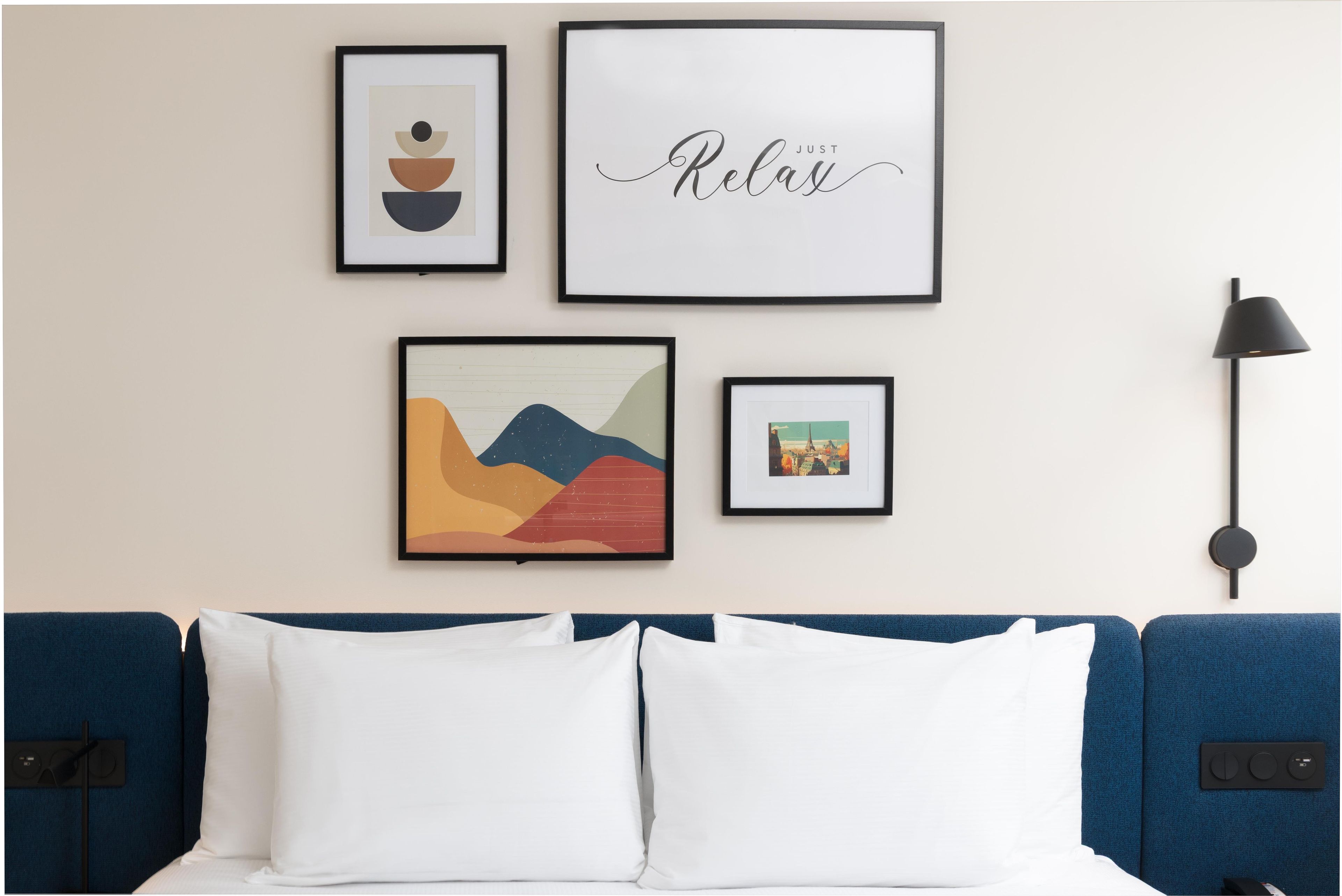 A hotel room with a bed, a wall-mounted lamp, and four framed artworks.