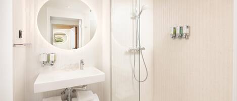 A modern bathroom with a glass-enclosed shower, a round mirror, a white sink, and a towel rack.
