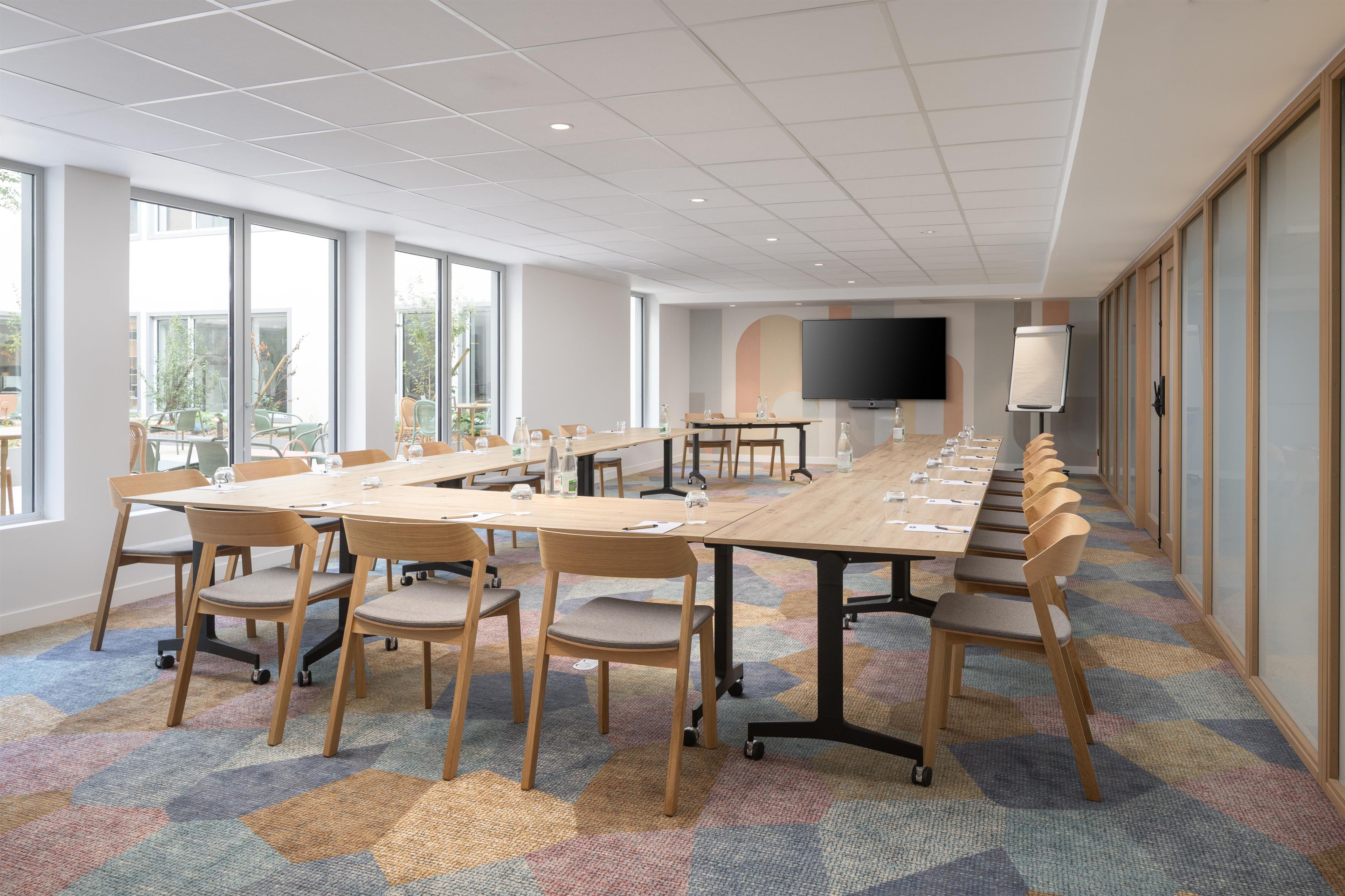A conference room with a long table, chairs, a large screen, and a view of the outdoors.