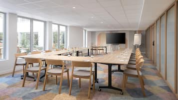 A conference room with a long table, chairs, a large screen, and a view of the outdoors.