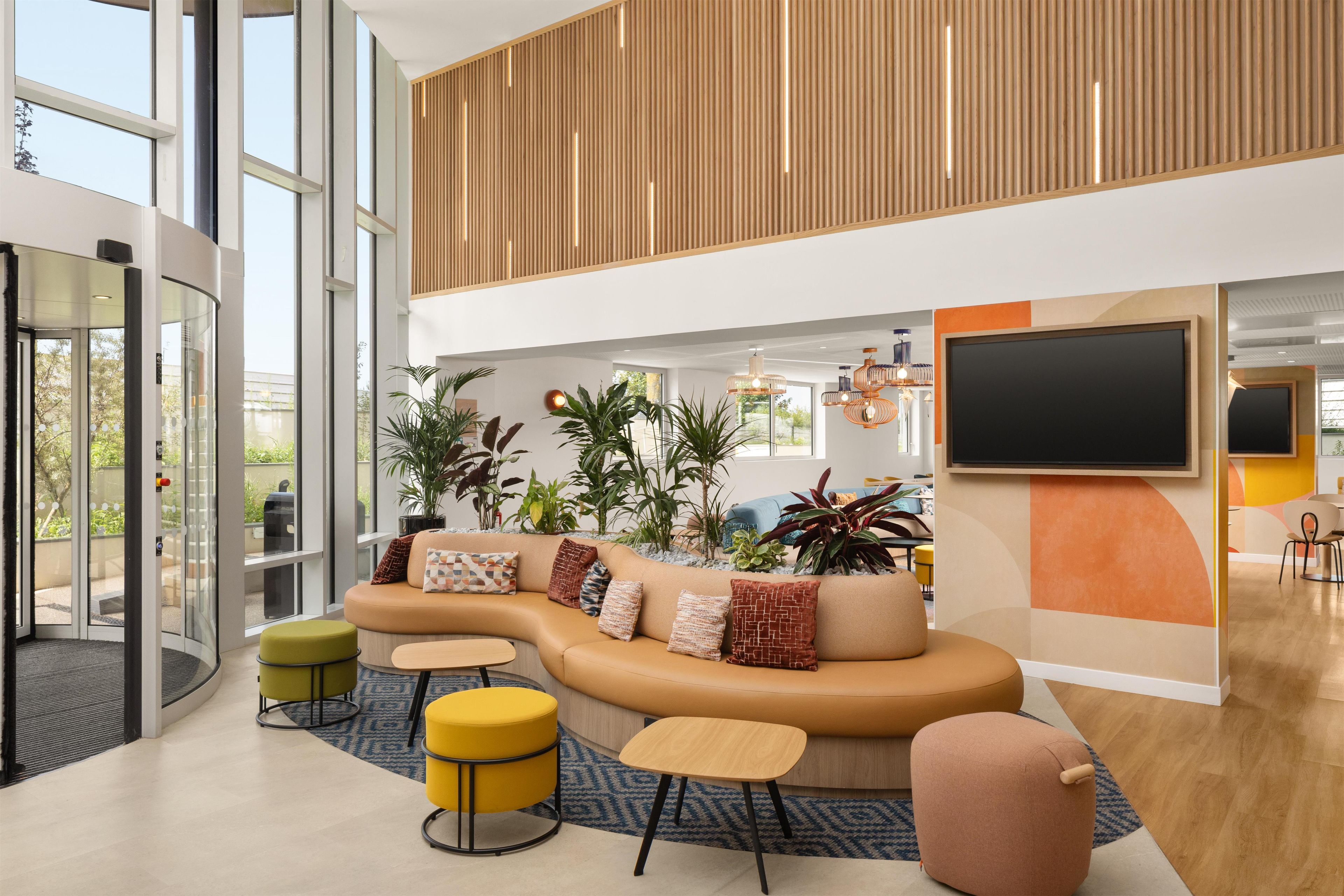 A modern lobby with a curved sofa, round ottomans, and a large TV screen.