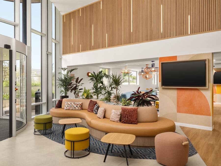 A modern lobby with a curved sofa, round ottomans, and a large TV screen.