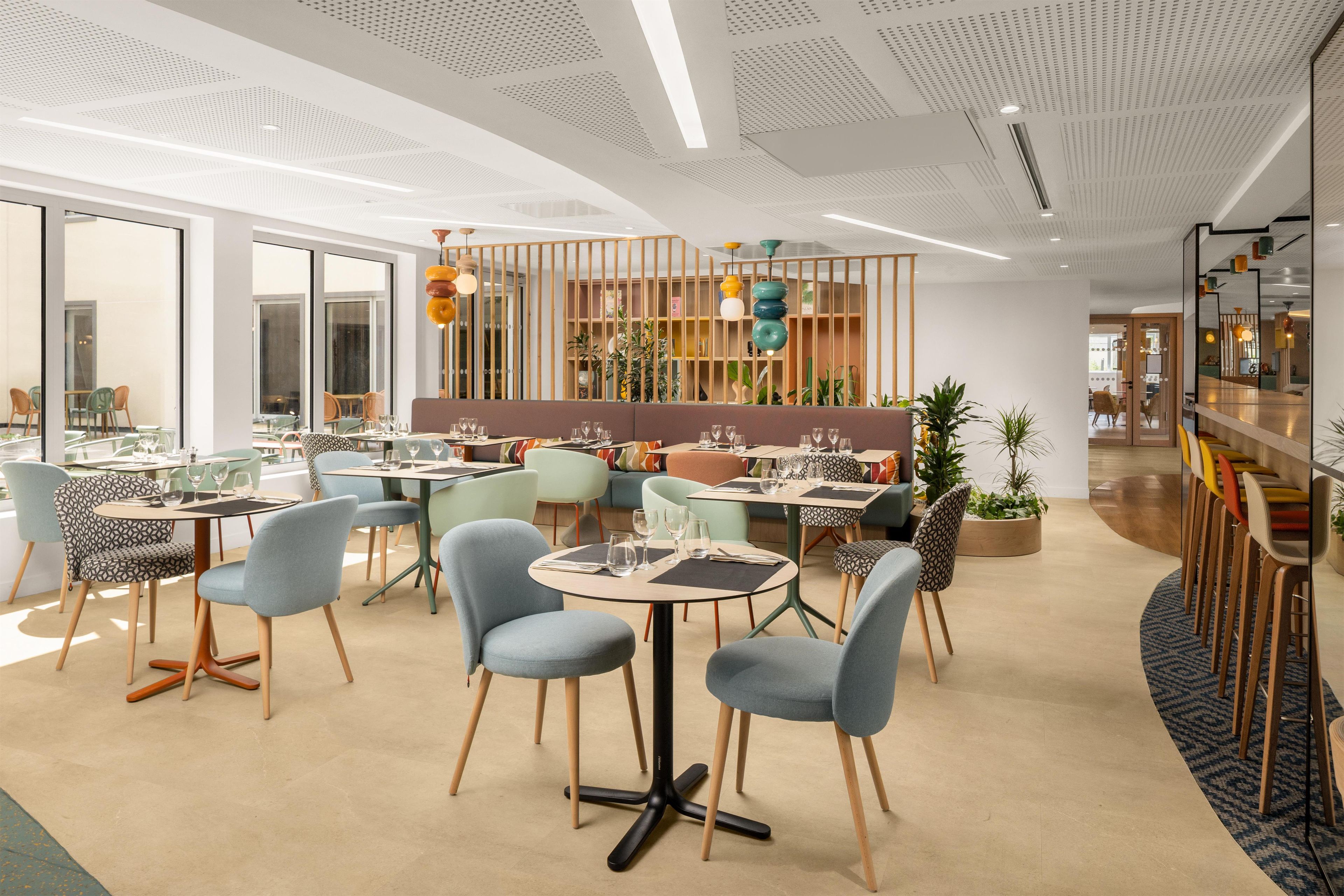 Uma área de refeições moderna com mesas e cadeiras redondas, um espaço de bar com banquetas e um teto com padrão único.