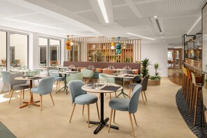 A modern dining area with round tables and chairs, a bar area with stools, and a ceiling with a unique pattern. - Hampton By Hilton Paris Charles De Gaulle Airport (Roissy-en-France)