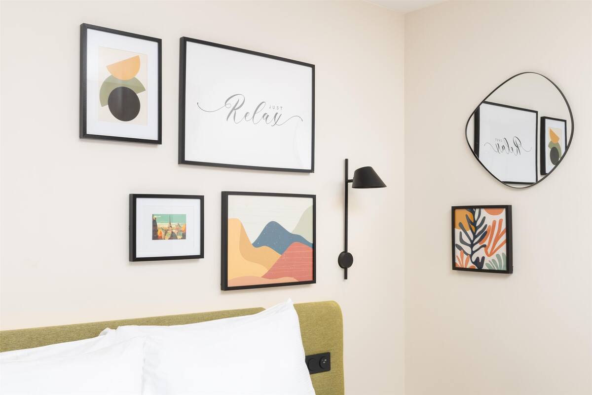 A hotel room with a bed, a wall-mounted lamp, and several framed artworks.