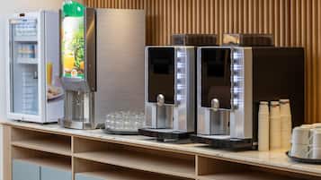 A self-service beverage station with a refrigerator, a juice dispenser, and two coffee machines.