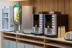 A self-service beverage station with a refrigerator, a juice dispenser, and two coffee machines. - Hampton By Hilton Paris Charles De Gaulle Airport (Roissy-en-France)