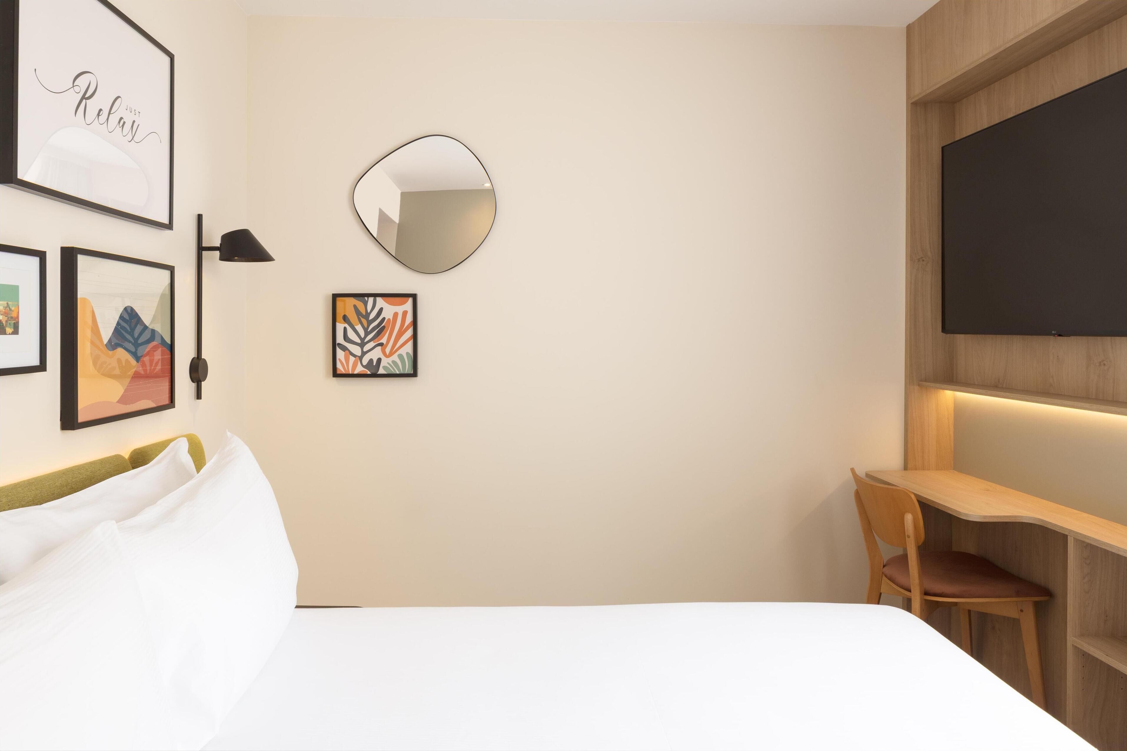 A modern hotel room with a bed, a desk, and a large mirror.