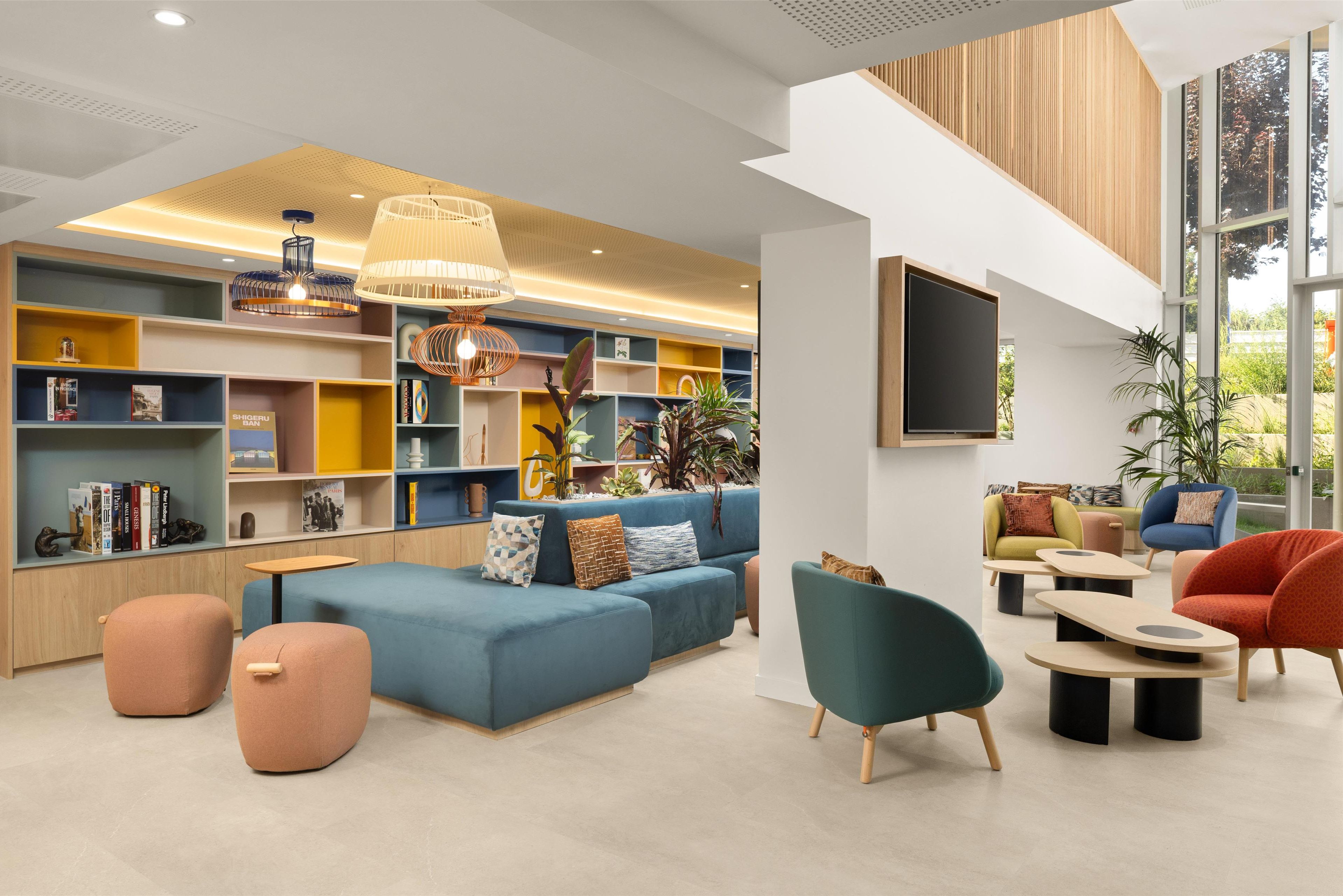 Un espacio lounge moderno con un sofá azul, sillones azul verdosos y varios estantes repletos de libros y objetos decorativos.
