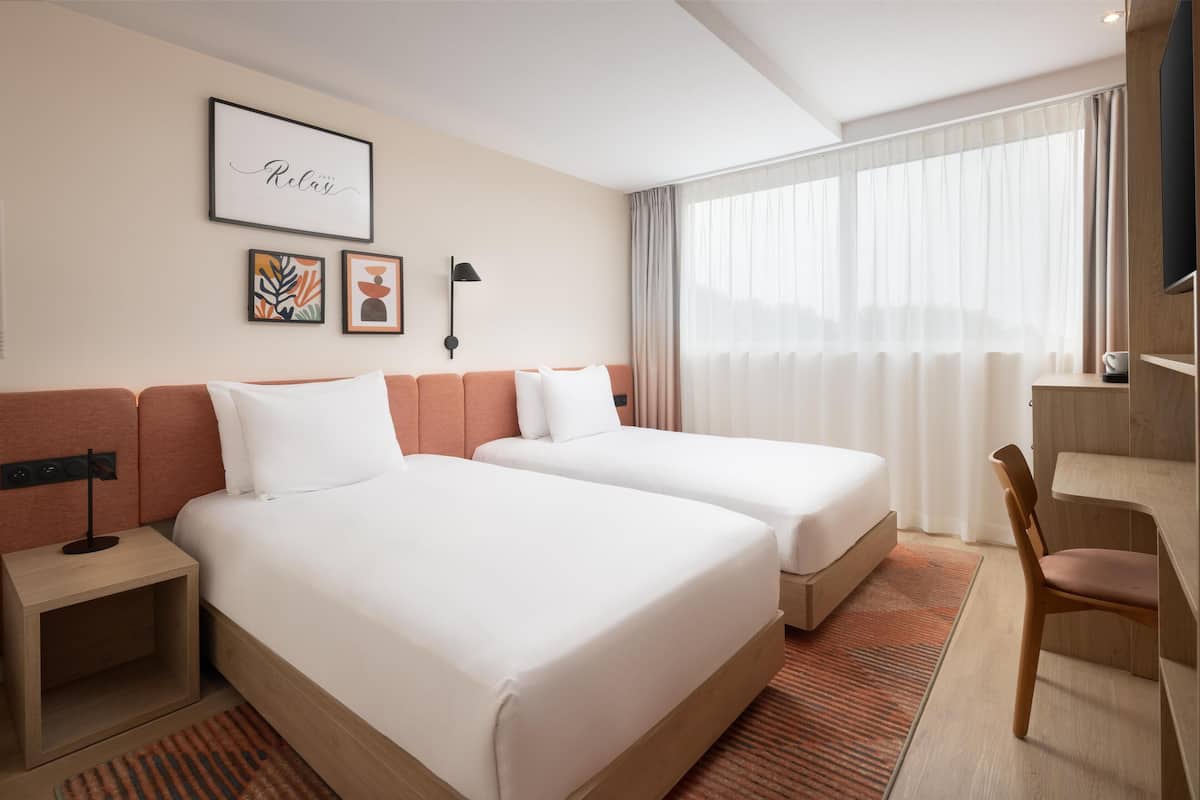A hotel room with two beds, a desk, a chair, and a TV.