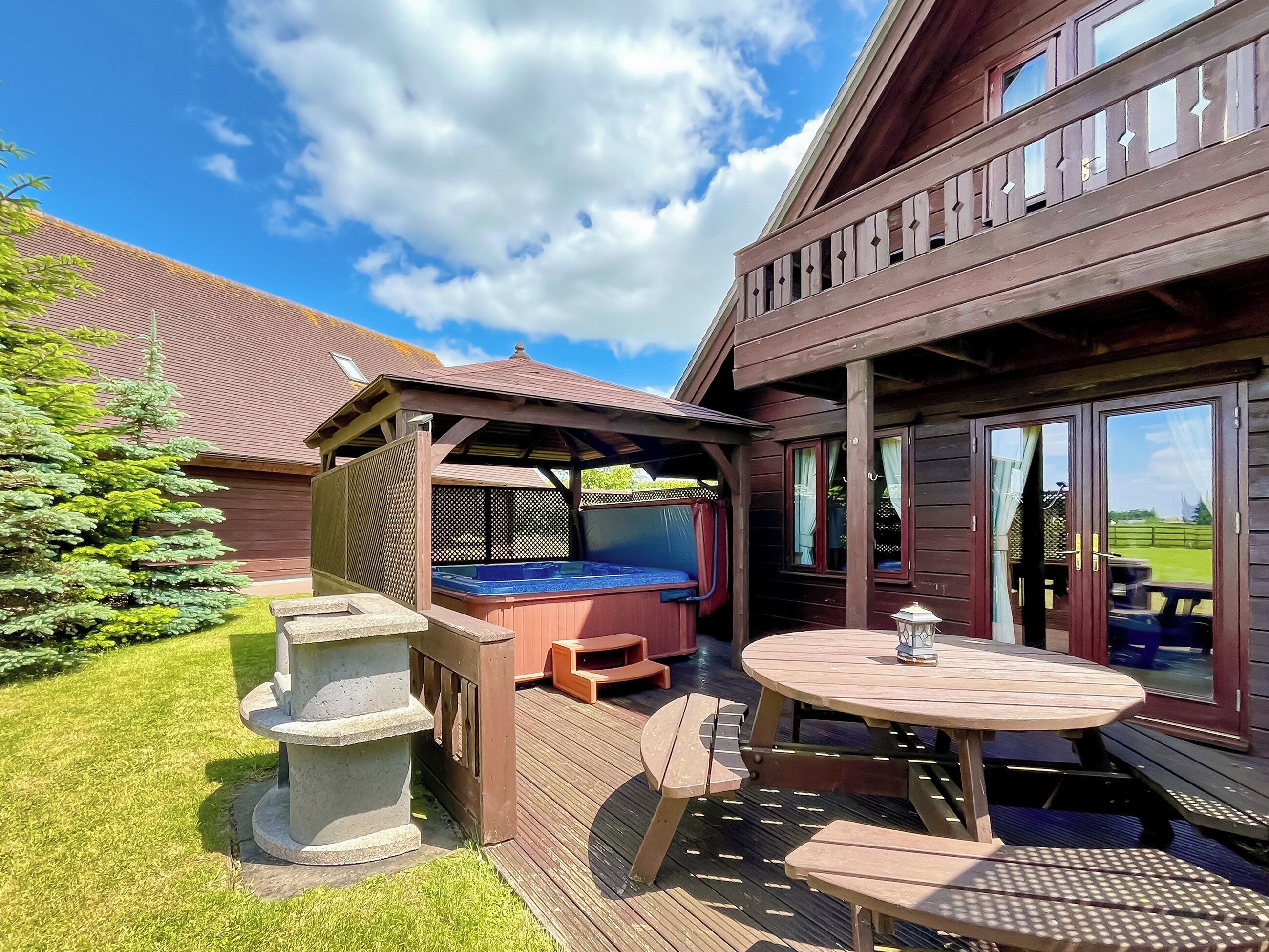 A wooden deck with a hot tub, outdoor seating, and a table.