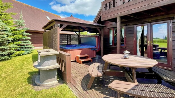 Une terrasse en bois avec un jacuzzi, des sièges d’extérieur et une table.