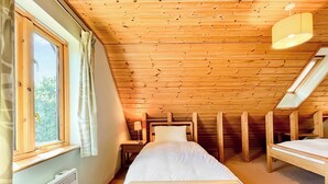 Une petite pièce agréable, avec un plafond en pente, un lit simple, une table de chevet et une fenêtre avec des rideaux.