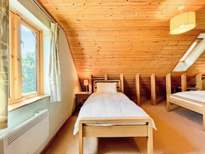 Een kleine, knusse kamer met schuine balken, een enkel bed, een nachtkastje en een raam met gordijnen.