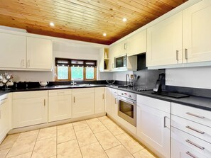 A modern kitchen with white cabinets, a black countertop, and a wooden ceiling.