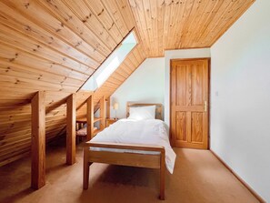 A bedroom with a sloped ceiling, wooden bed frame, and a door.