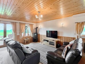 A cozy living room with a fireplace, leather sofas, a flat-screen TV, and a large window with curtains.