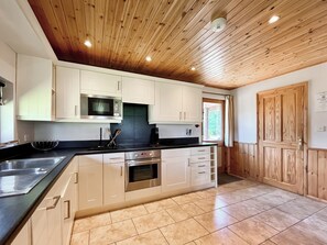 A modern kitchen with wooden ceiling, stainless steel appliances, and a black countertop.