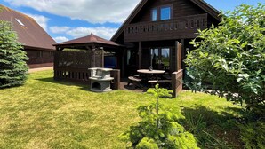 Une cabane en bois dotée d’un patio couvert, d’une cheminée en pierre et d’une pelouse bien entretenue.