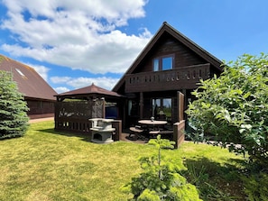 Een houten chalet met een overdekt terras, een stenen openhaard en een verzorgd gazon.
