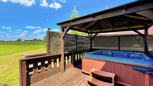 Une terrasse en bois avec un jacuzzi et des sièges, entourée d’une clôture et offrant une vue sur un ciel dégagé.
