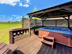 Een houten terras met een jacuzzi en zitplaatsen, omringd door een hek en een heldere lucht.