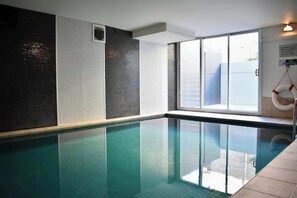 Una piscina con agua cristalina, un muro de cristal y un flotador salvavidas a la derecha.