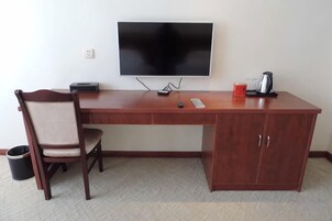 Escritorio de madera con televisor de pantalla plana, una silla, un cesto de basura y una cafetera.
