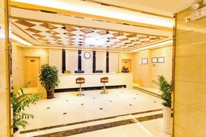 A lobby with a reception desk, two bar stools, a clock, framed pictures on the wall, and potted plants. - Anmen Lijiang Inn (Qimen)