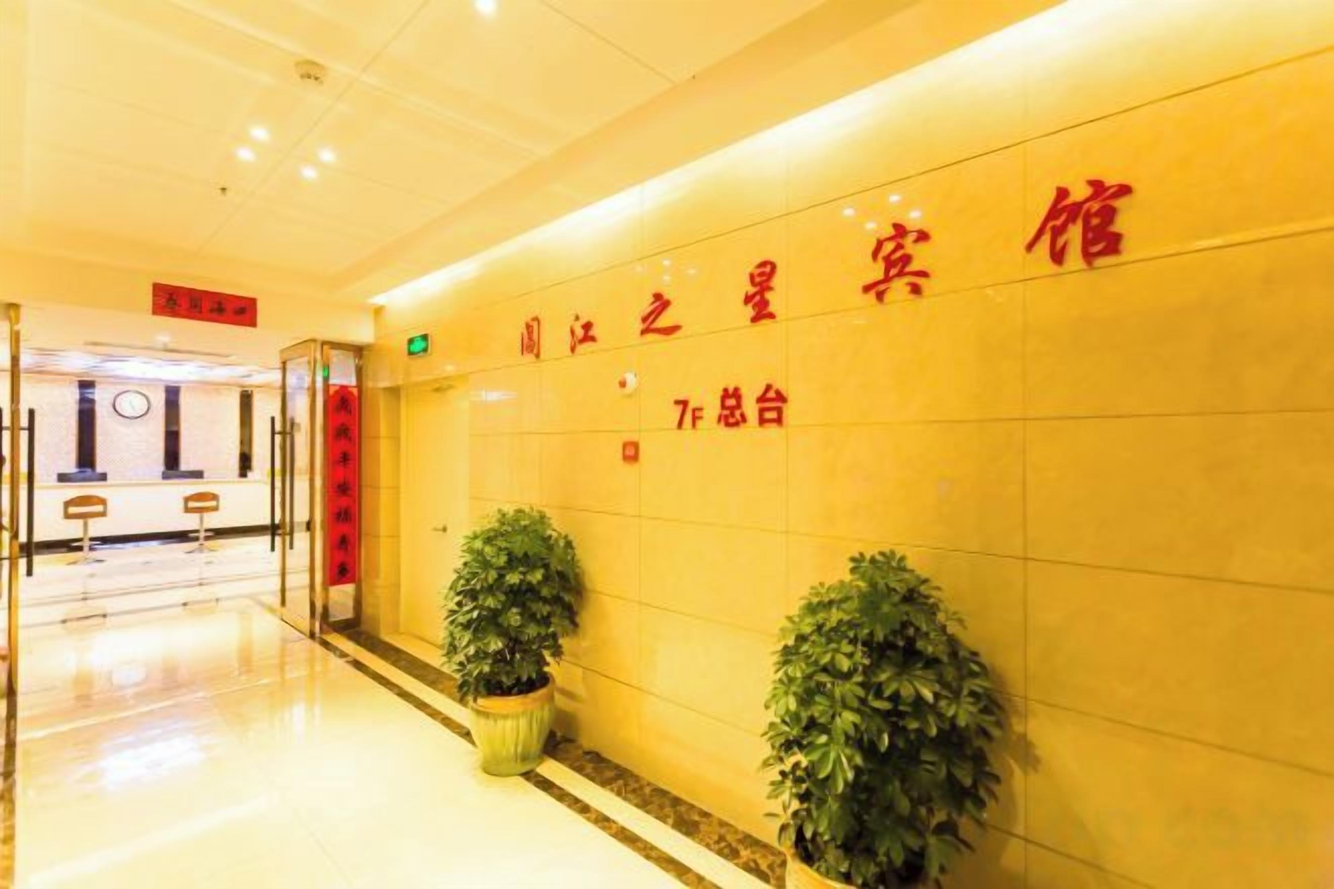 A hotel reception area with a reception desk, a wall with signage, and potted plants.
