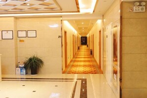A hotel hallway with a carpeted floor, framed certificates on the wall, and a potted plant. - Anmen Lijiang Inn (Qimen)