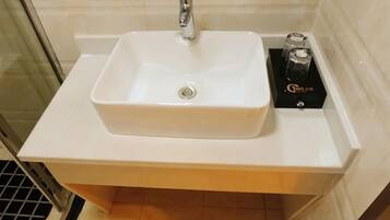 A white rectangular sink with a single faucet, a black box with gold lettering, and a tiled wall in the background.
