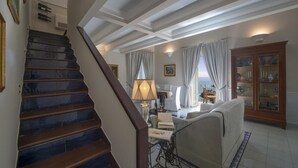 Un escalier mène à un espace de vie comprenant un canapé, une table et une vue sur la mer.