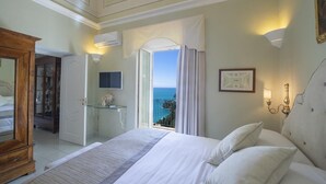Une chambre avec un grand lit, un bureau en verre, une télévision et une vue sur la mer.