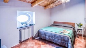 A bedroom with a bed, a window with a circular light, a radiator, and a small bedside table with a plant. - Casa Centrale in central Sorrento (Sorrento)
