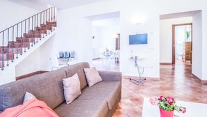 A modern living room with a sofa, a staircase, a dining area, and a TV mounted on the wall. - Casa Centrale in central Sorrento (Sorrento)