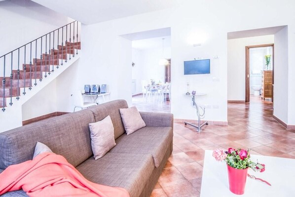 A modern living room with a sofa, a staircase, a dining area, and a TV mounted on the wall. - Casa Centrale in central Sorrento (Sorrento)