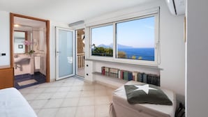 Une chambre avec une grande fenêtre, un lit, une table de chevet et une vue sur la mer.
