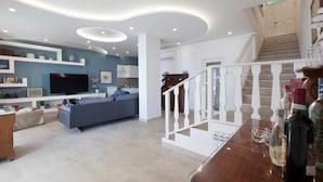 Un salon moderne avec un canapé gris, un téléviseur et un escalier menant à l’étage supérieur.