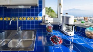 Une cuisine avec des carreaux bleus, un évier en acier inoxydable, une machine à café et une vue sur la mer.