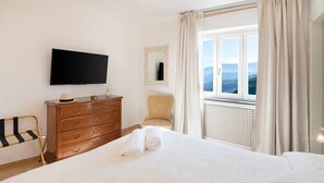 Une chambre d’hôtel avec un grand lit, une commode en bois, un téléviseur, une chaise et une vue sur l’extérieur par une fenêtre.