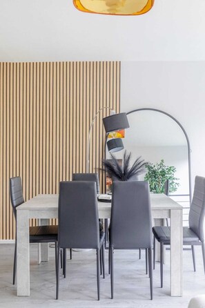 A modern dining area with a white table and black chairs, a tall floor lamp, and a vertical wooden panel in the background.