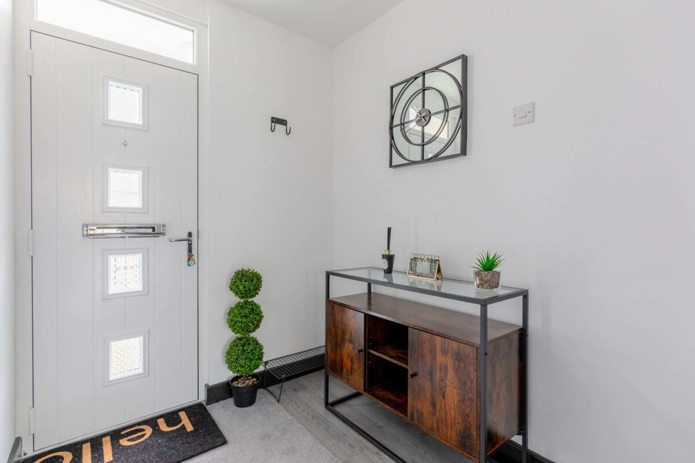 A modern hallway with a white door, a glass console table with decorative items, and a small potted plant.