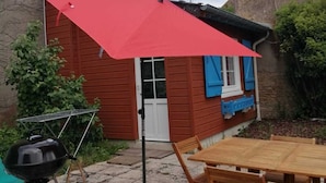 Eine Holzterrasse mit einem roten Sonnenschirm, einem Grill und einem Holztisch.
