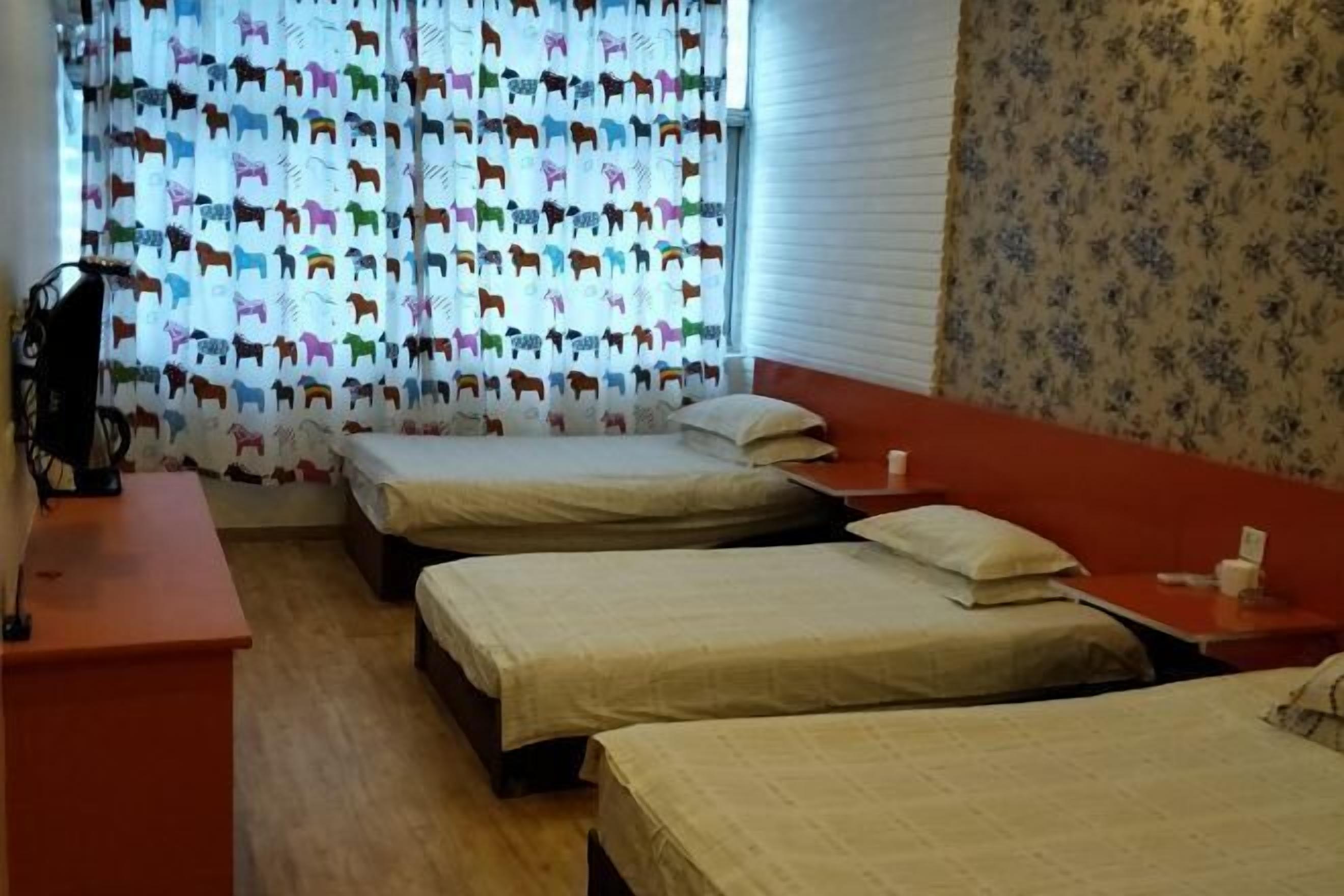 A room with three beds, a desk, and a window with patterned curtains.