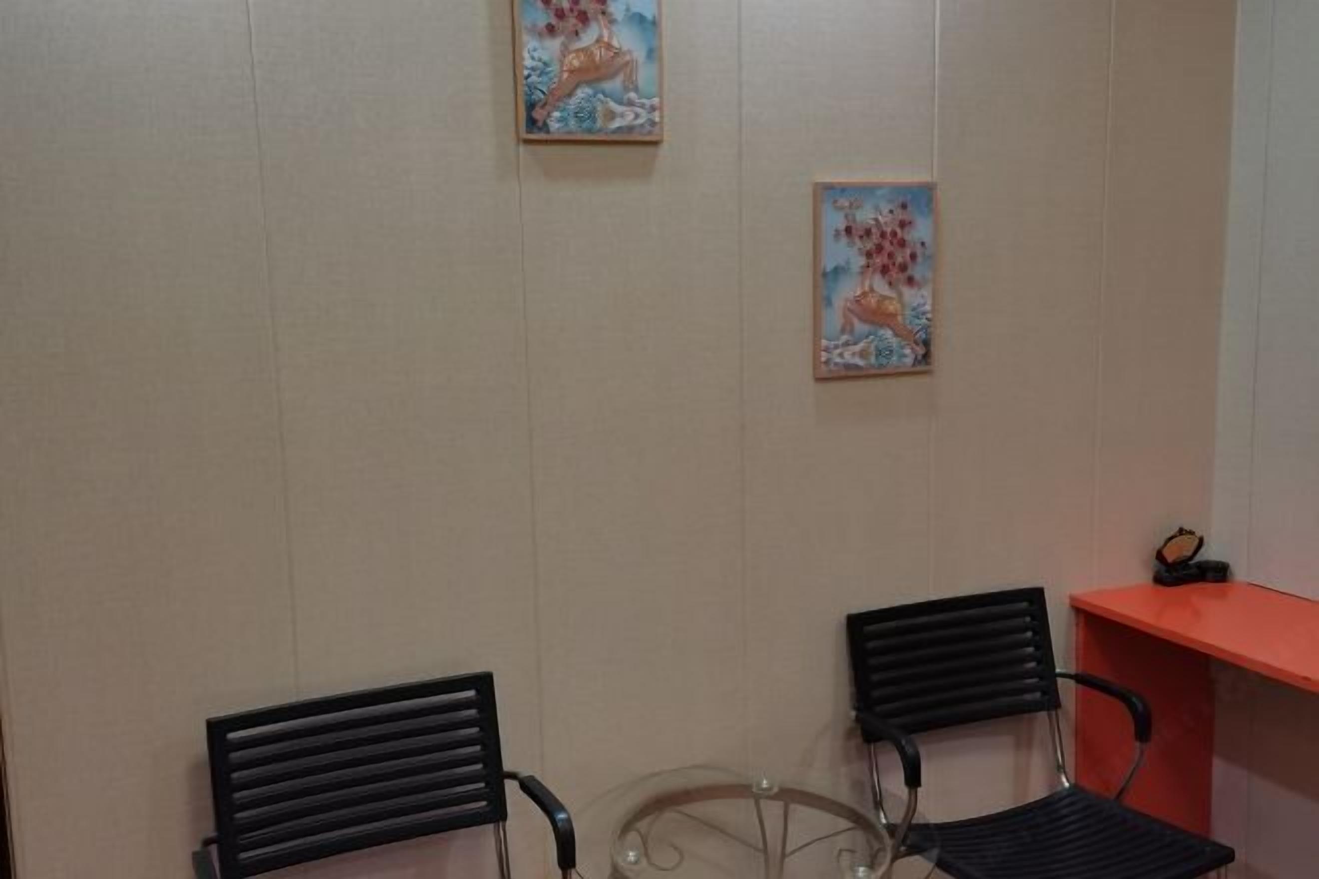 A room with two black chairs, a small round table, and two wall-mounted paintings.