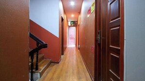 Un couloir étroit au plancher en bois, avec un escalier sur la gauche et une porte sur la droite.