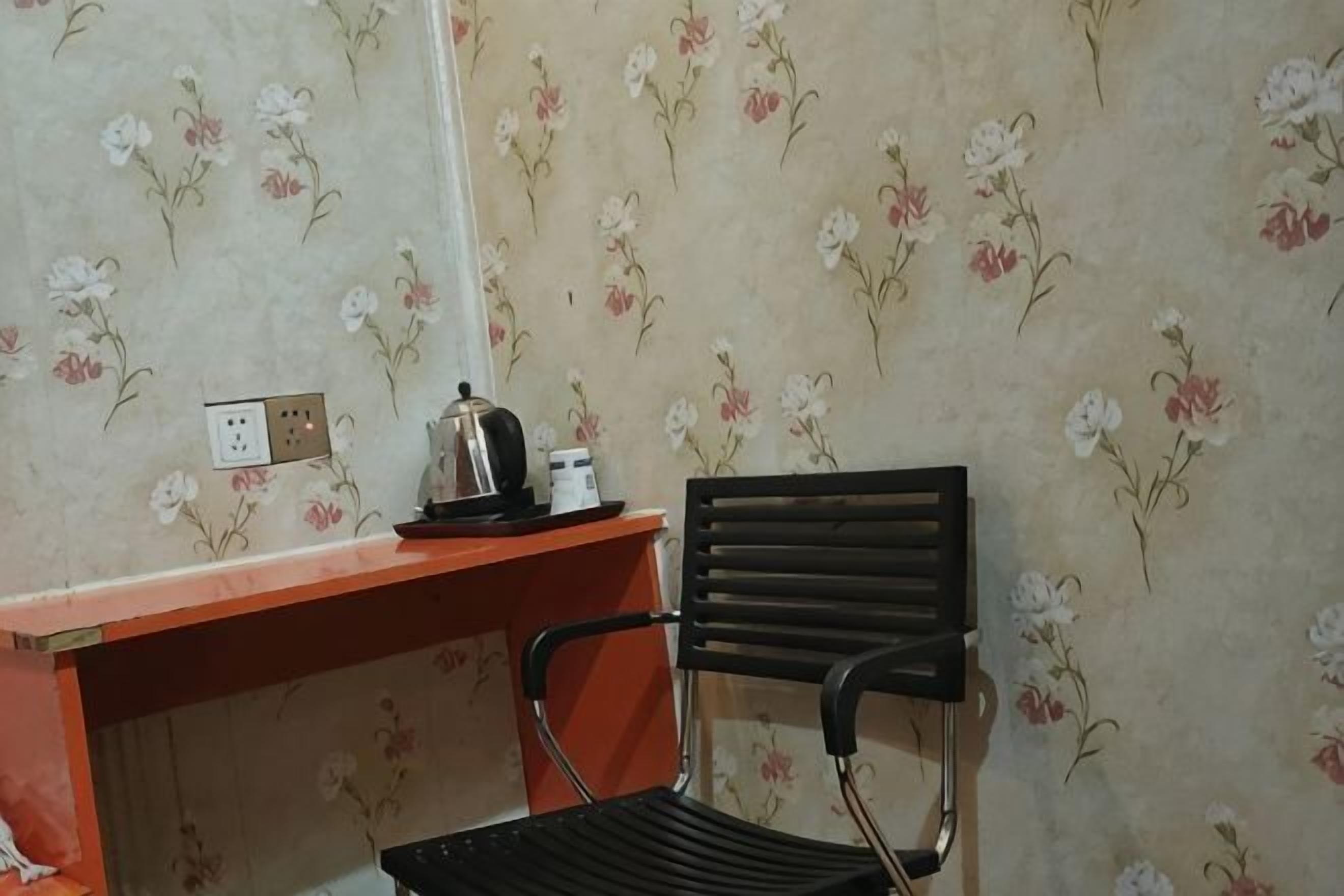 A room with a floral wallpaper, a red desk with a kettle, and a black chair.