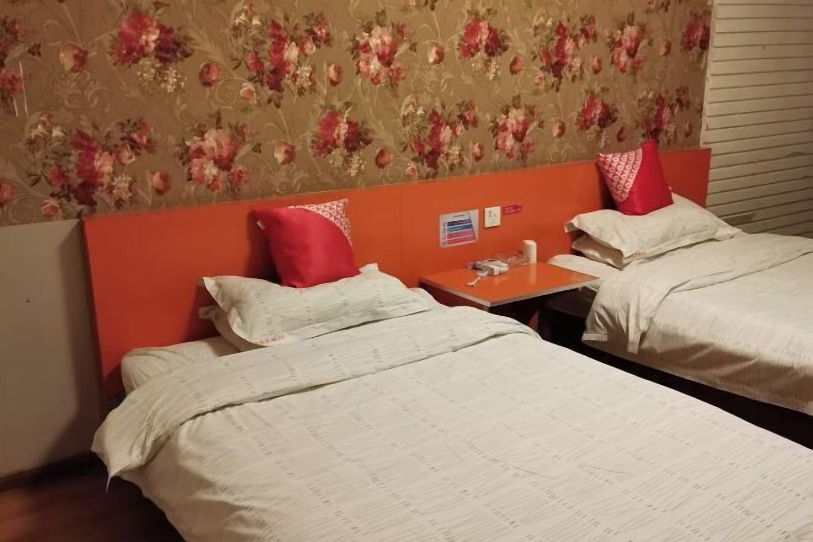 A hotel room with two beds, floral wallpaper, a red headboard, and a small table with a flag and a calendar.